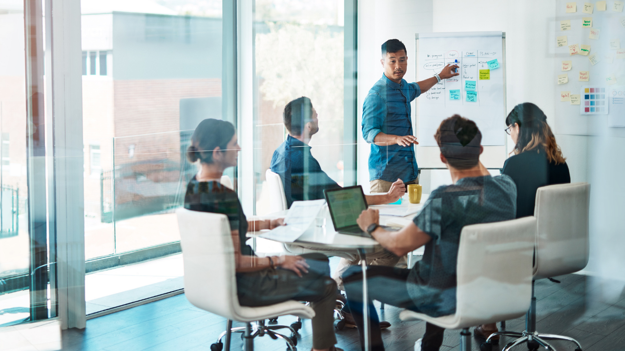 A team in a meeting room working through a plan on a whiteboard